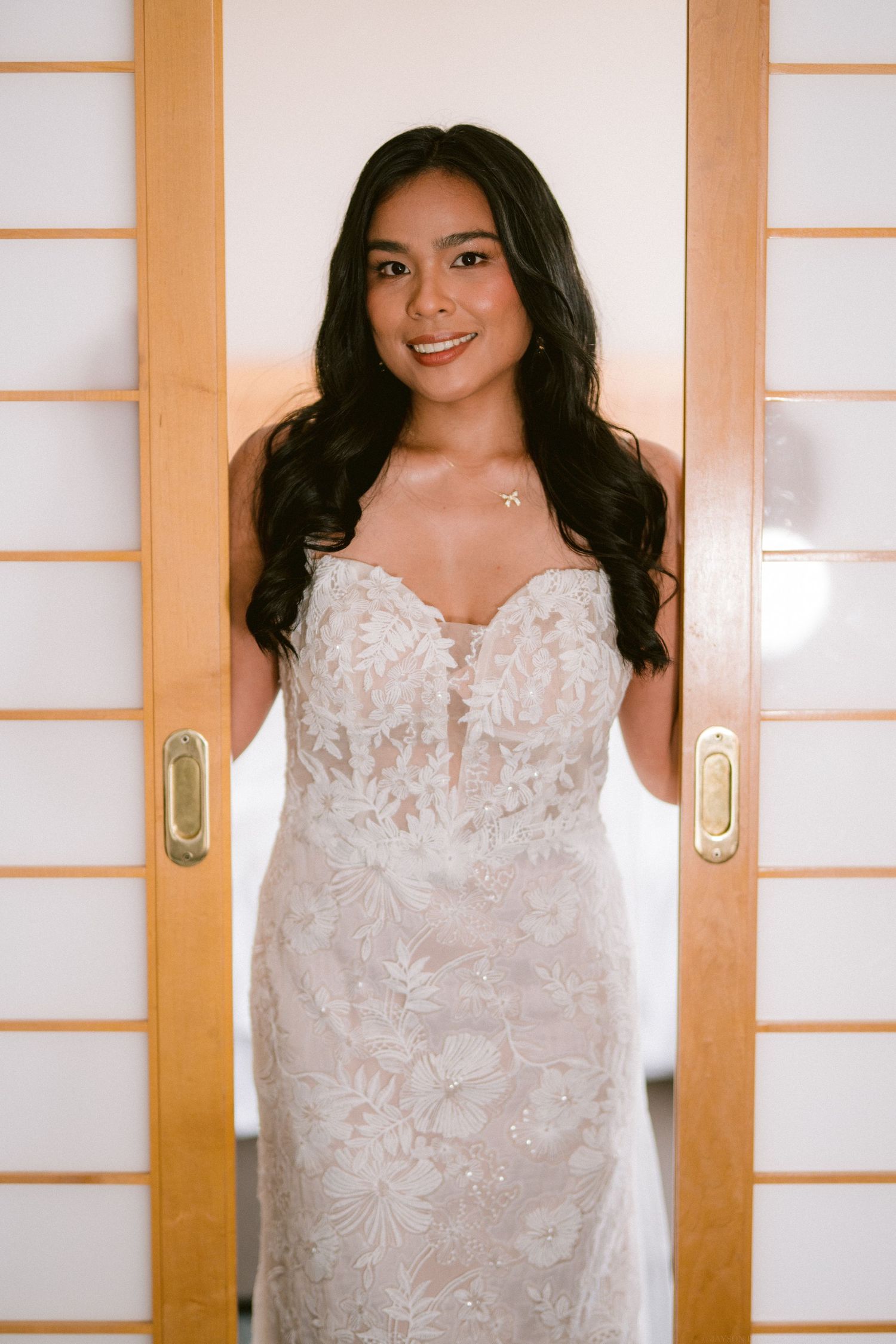 Bride wearing an elegant white lace wedding dress standing between sliding doors.