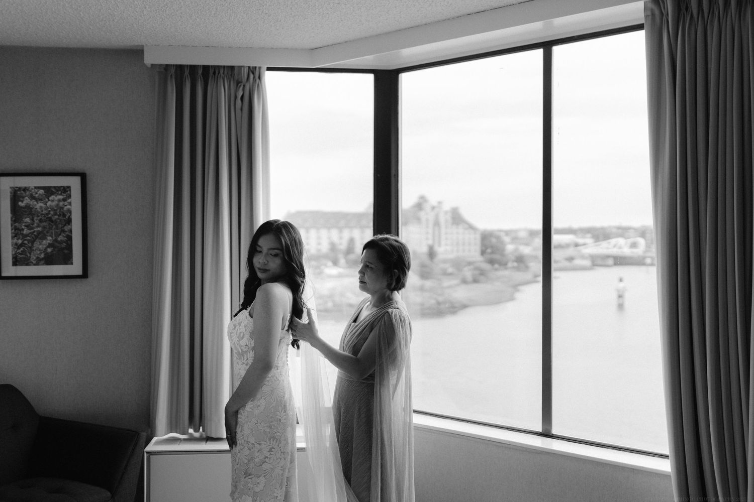Two people preparing by window with cityscape view in black and white.