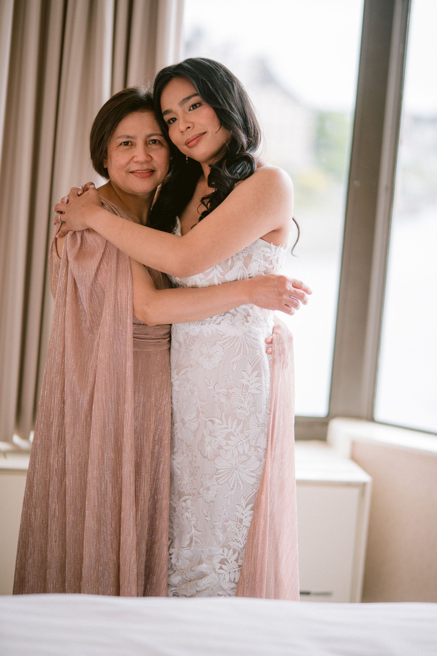 A touching moment between two women in soft pink and white dresses embracing.