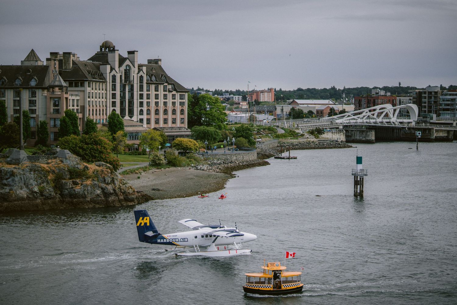 Waterfront cityscape with boat passing historic buildings and bridge in overcast weather.