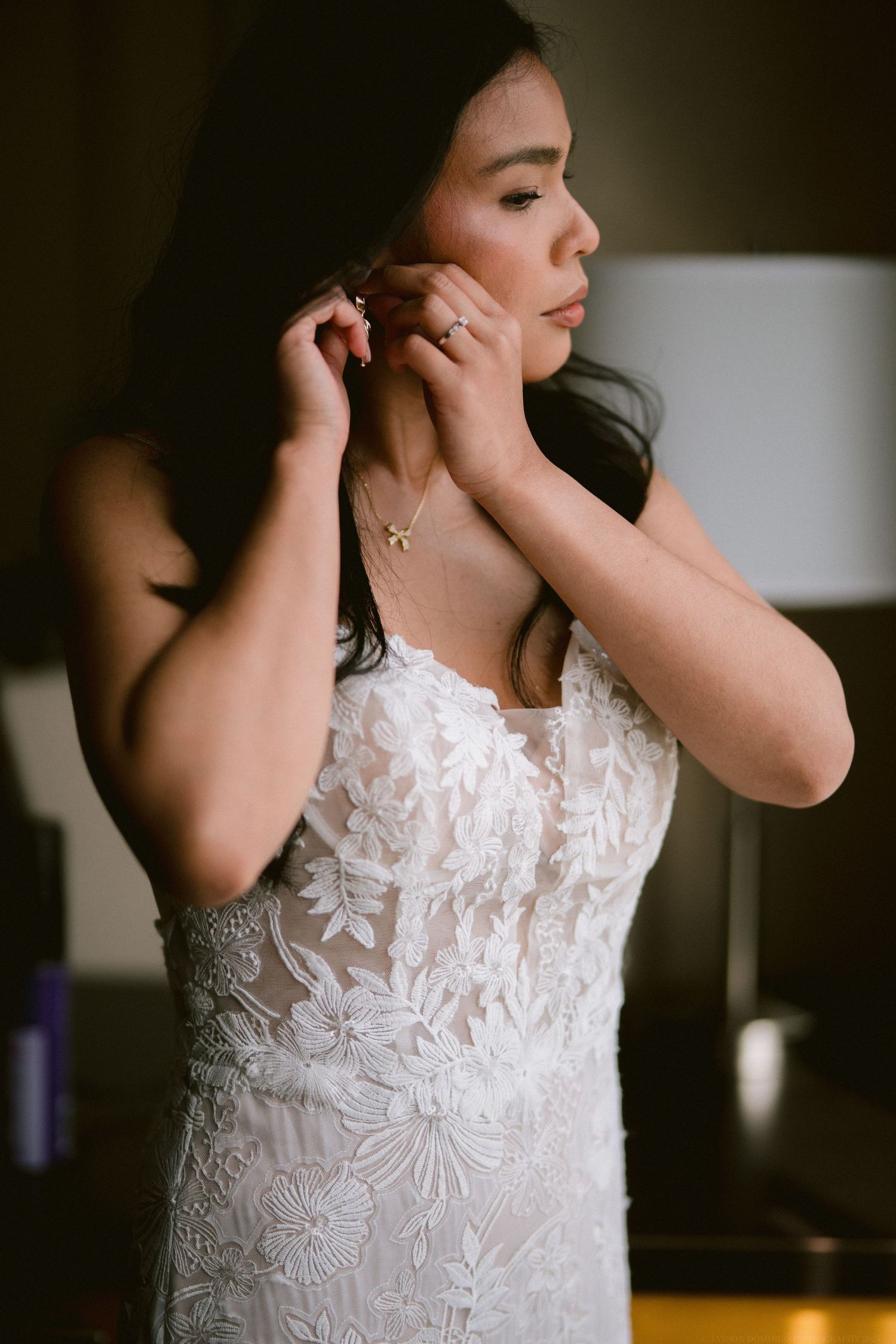 Close-up shot of a bride in a lace wedding dress putting on earrings.
