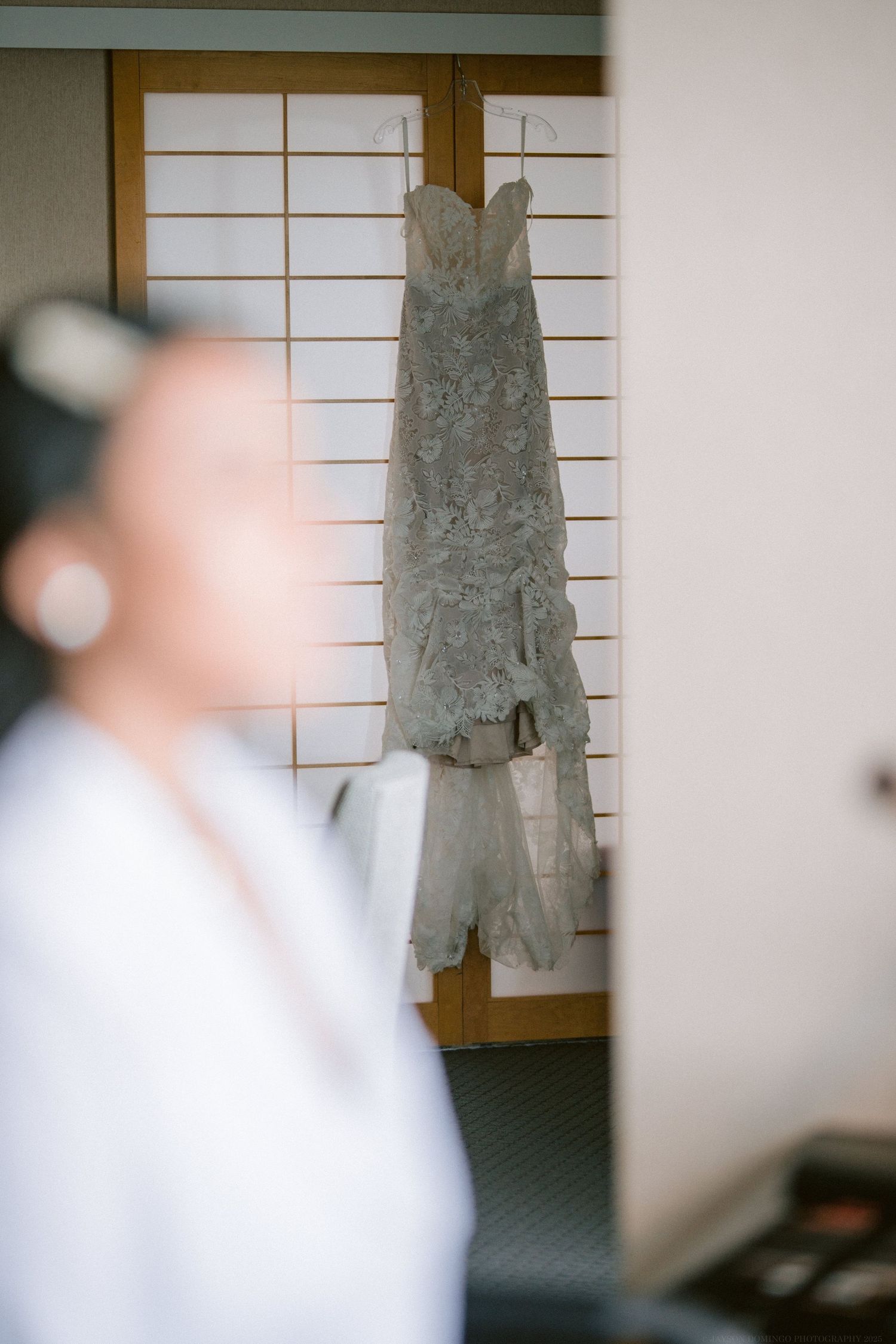 A delicate lace wedding dress hangs on display against traditional Japanese shoji screens.