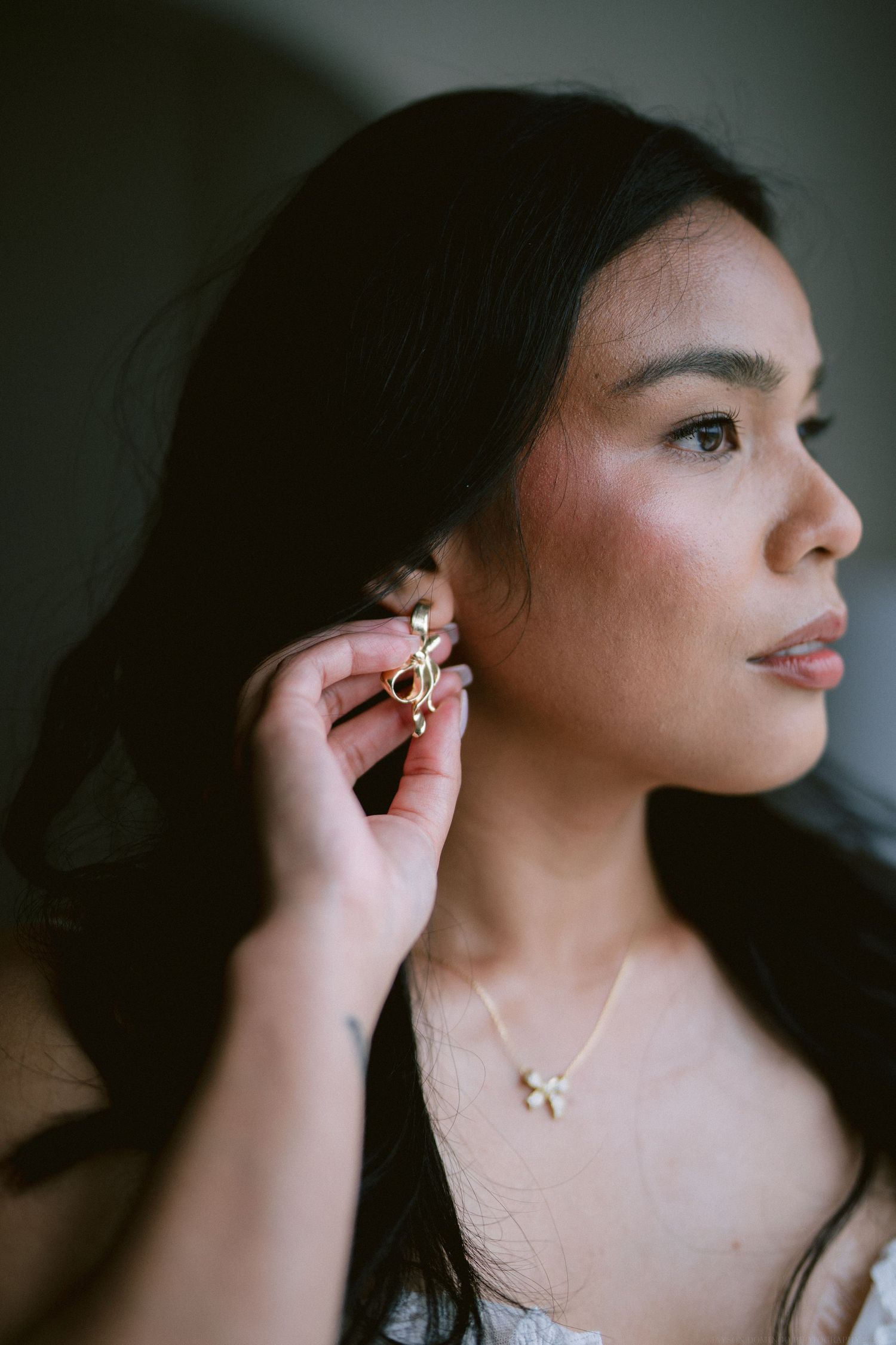 Elegant side profile portrait showing delicate jewelry and soft lighting.
