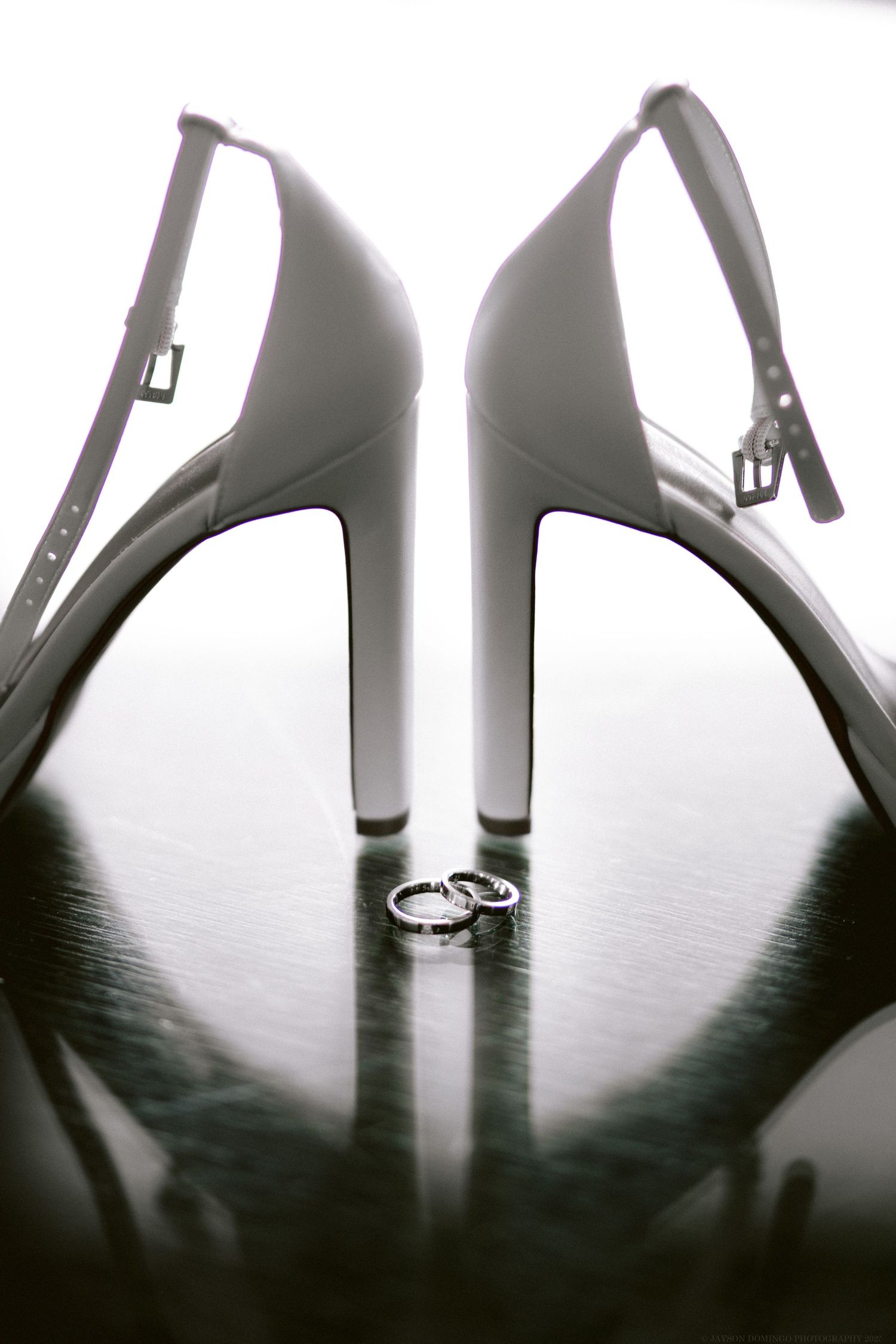 White high heel wedding shoes frame wedding rings in an artistic black and white composition.