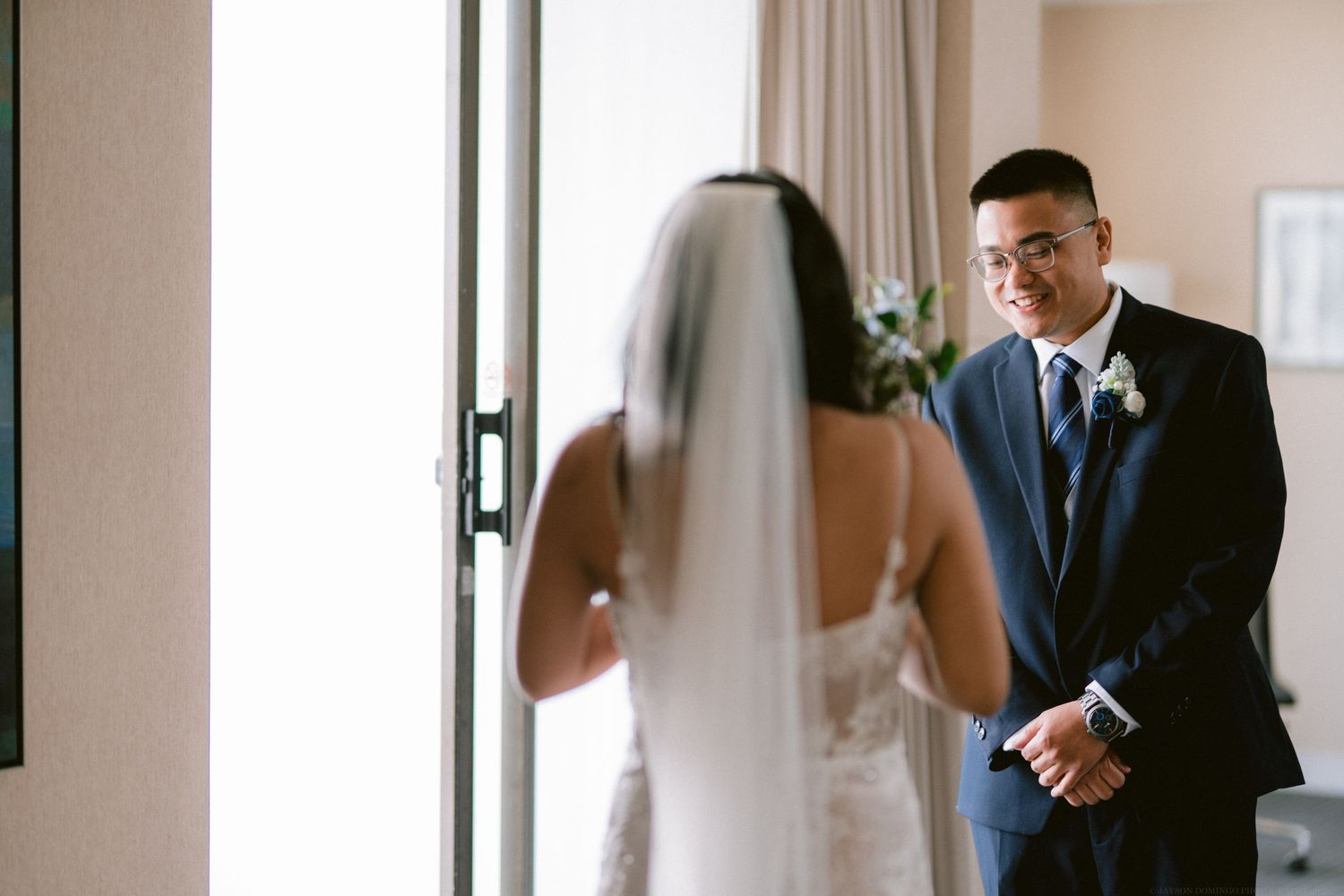 A first look moment captured in a hotel room with natural window light.