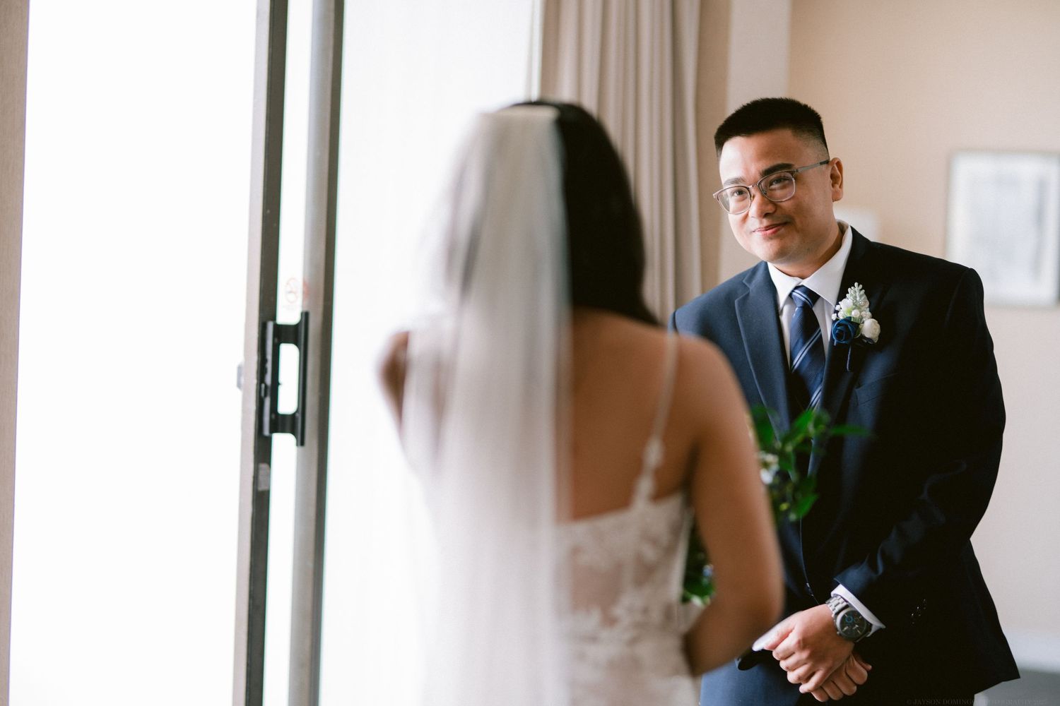 A tender first look moment between bride and groom by a window.