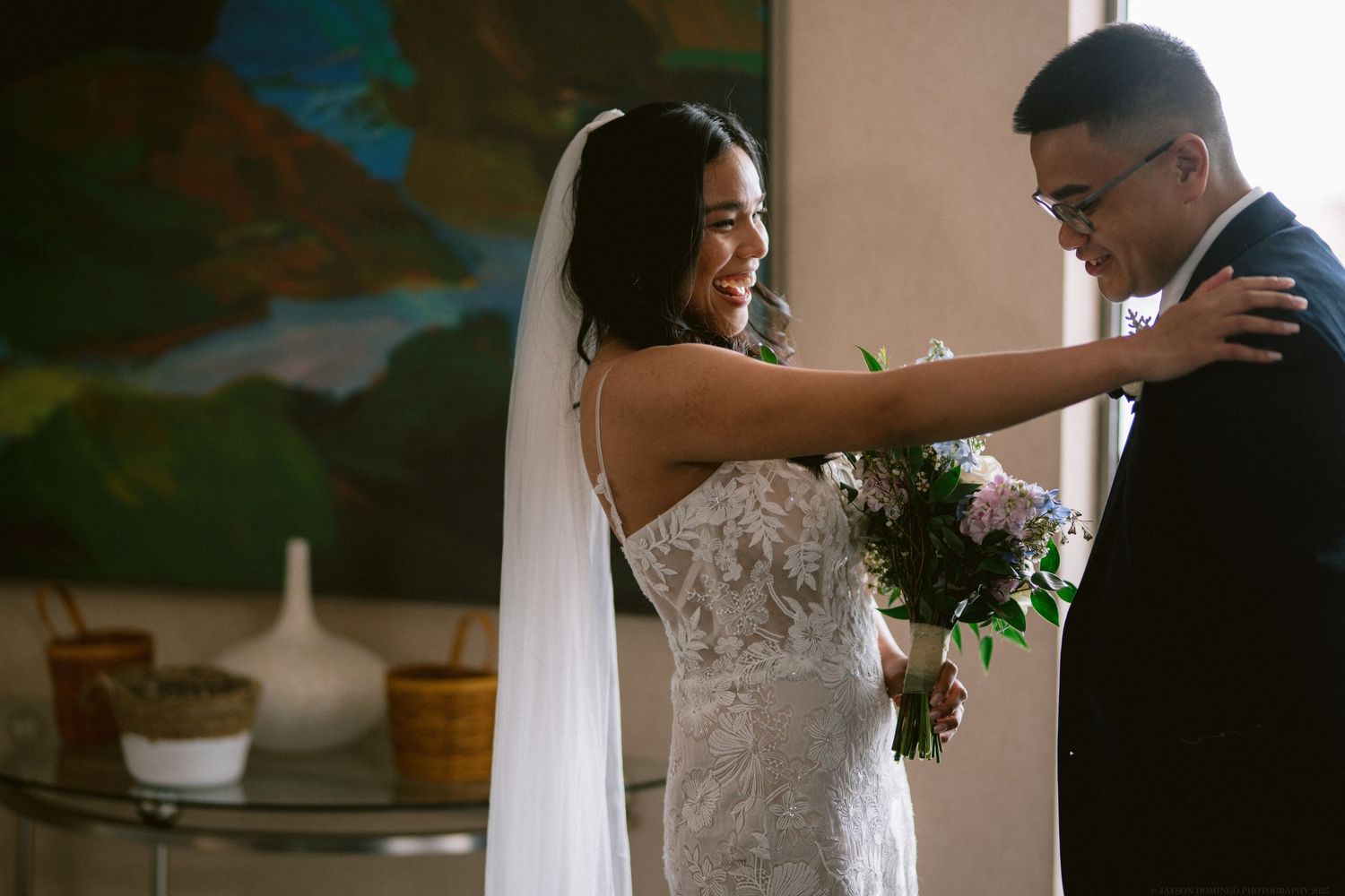 A tender moment between newlyweds sharing their first dance in front of a decorative wall.
