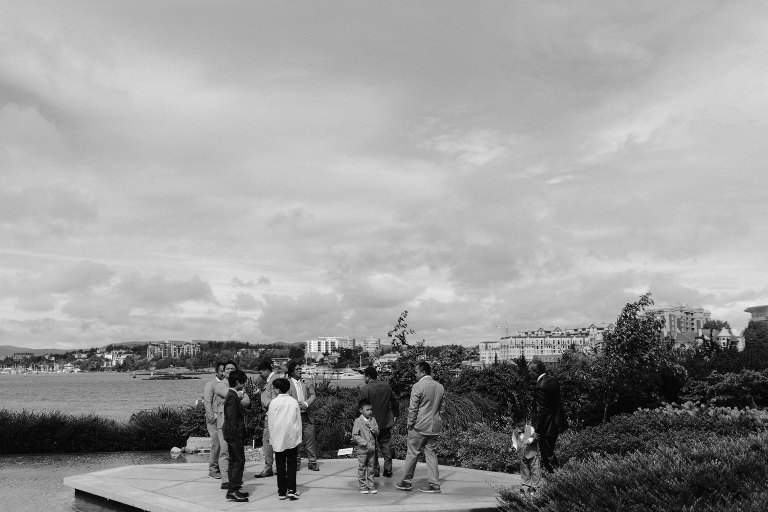 Wedding guests gather on a waterfront boardwalk under cloudy skies.