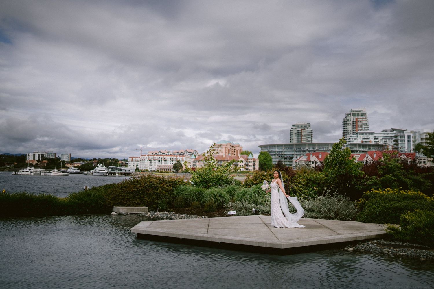 A dramatic wedding photo with cityscape and water views under moody clouds.