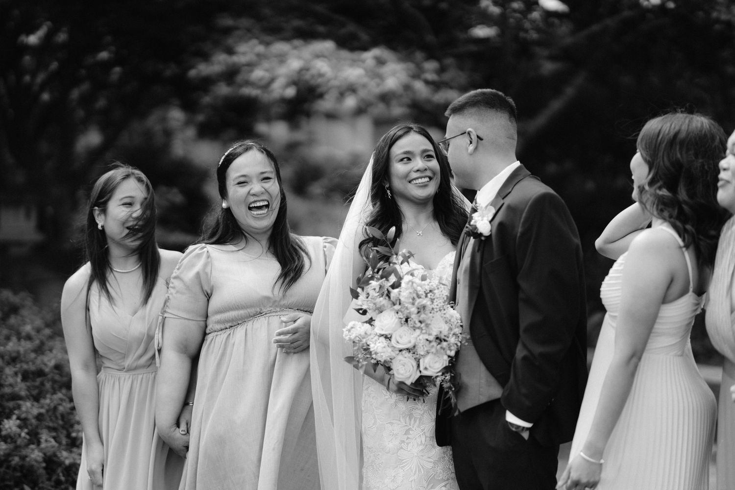 A joyful wedding party laughs together outdoors during wedding day celebrations.