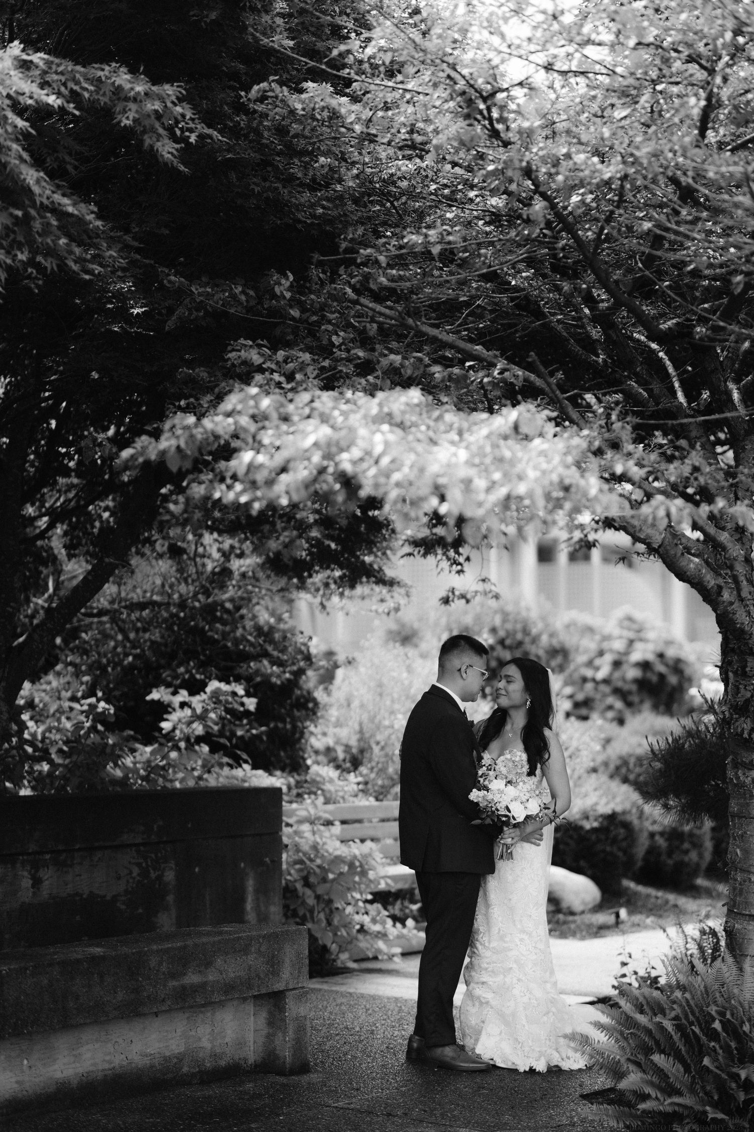 A romantic black and white wedding portrait under blooming trees in a garden setting.