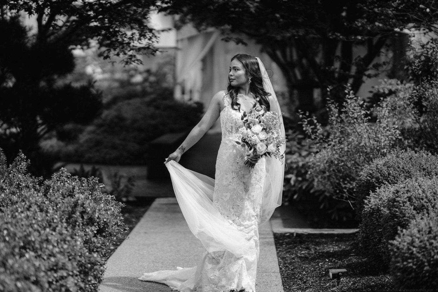 Black and white portrait of bride twirling her dress on a garden pathway.