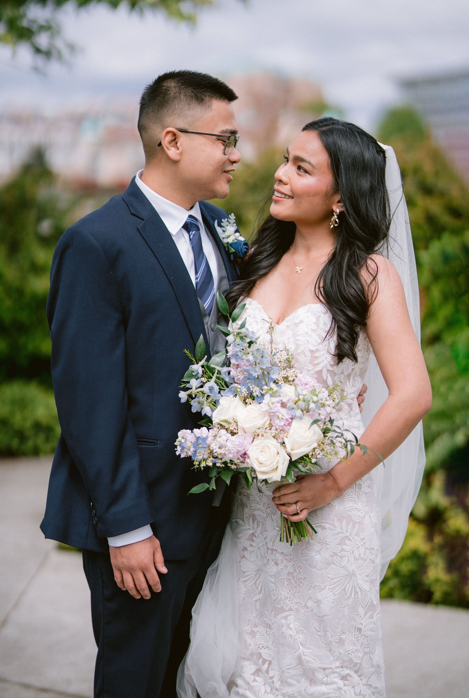 A newlywed couple shares an intimate moment while holding a purple and white floral bouquet.