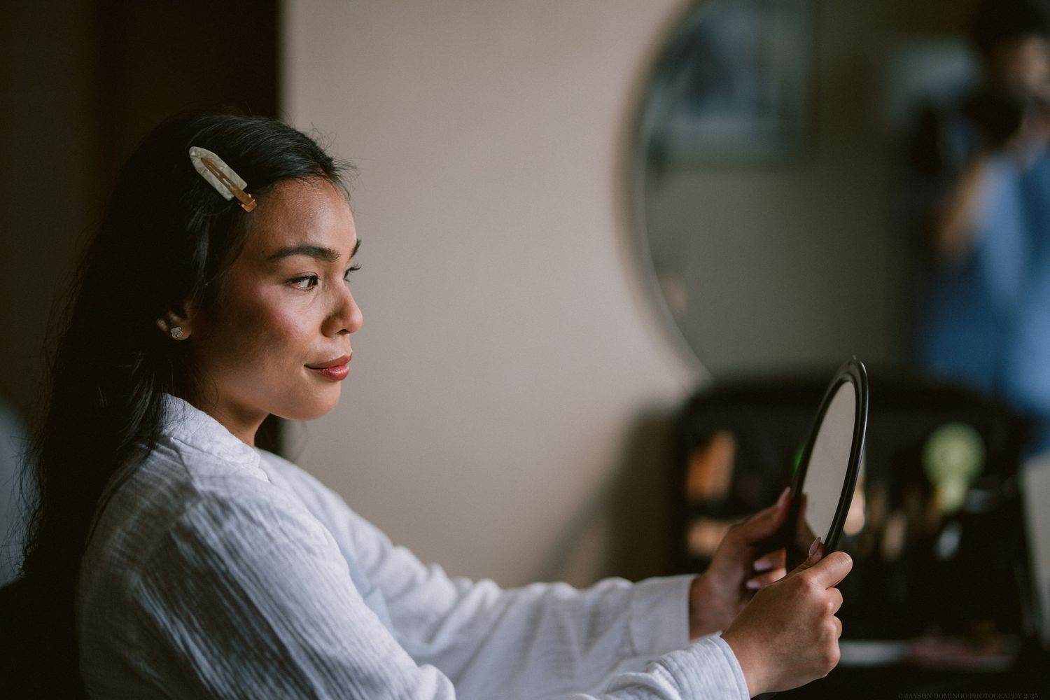 Person in white robe looking in mirror during wedding preparation.