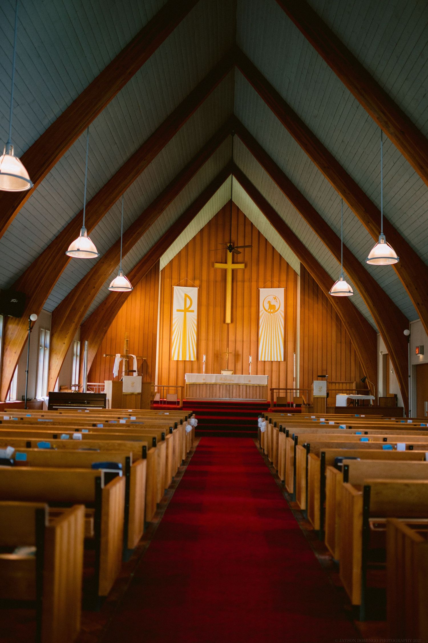 Interior view of a traditional church sanctuary with wooden pews and vaulted ceiling along a red carpet aisle.