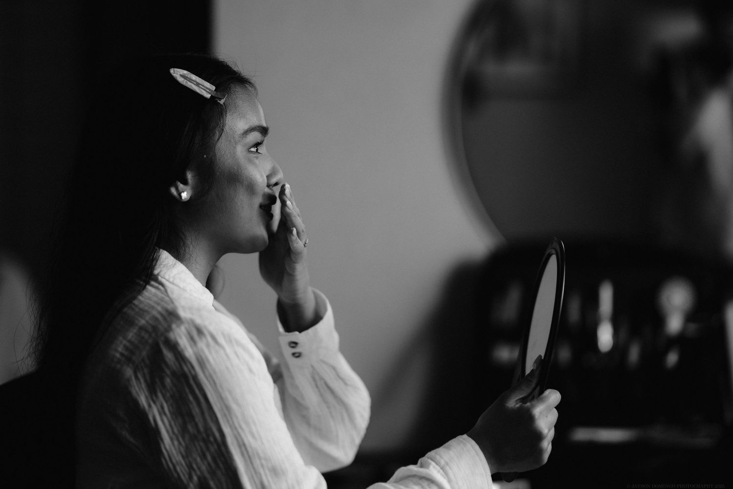 Black and white portrait of person holding mirror during preparation.