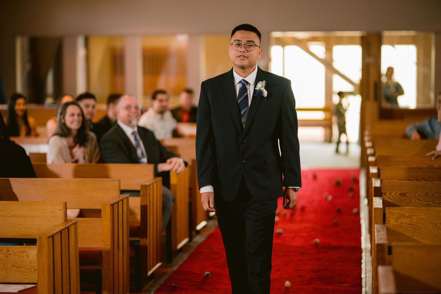 Person walking down the center aisle of a church wearing formal attire.