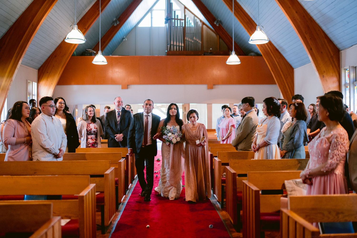 Wedding ceremony in progress inside a church with wooden arches and red carpet.