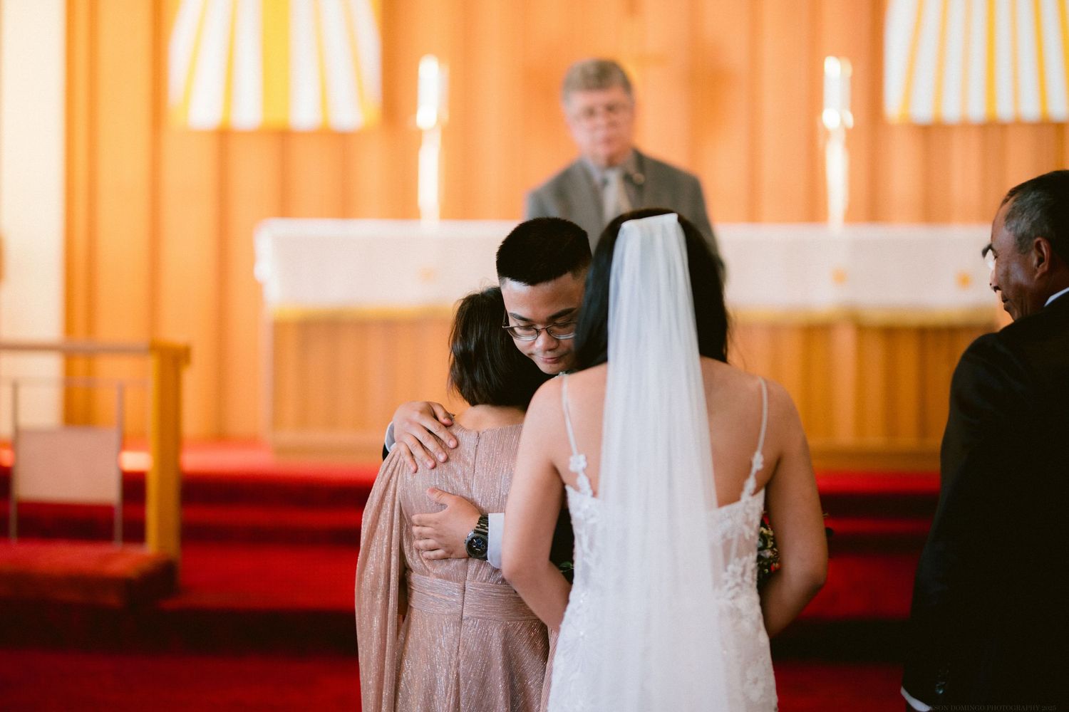 A touching moment during a wedding ceremony in a church with red carpet.