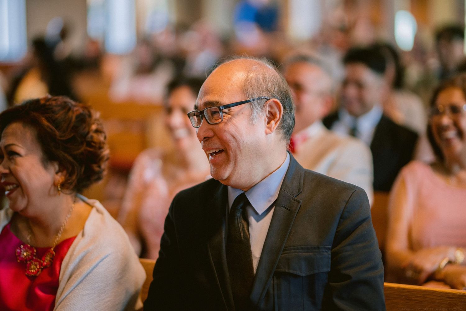 Wedding guests smile and laugh during ceremony in church pews.