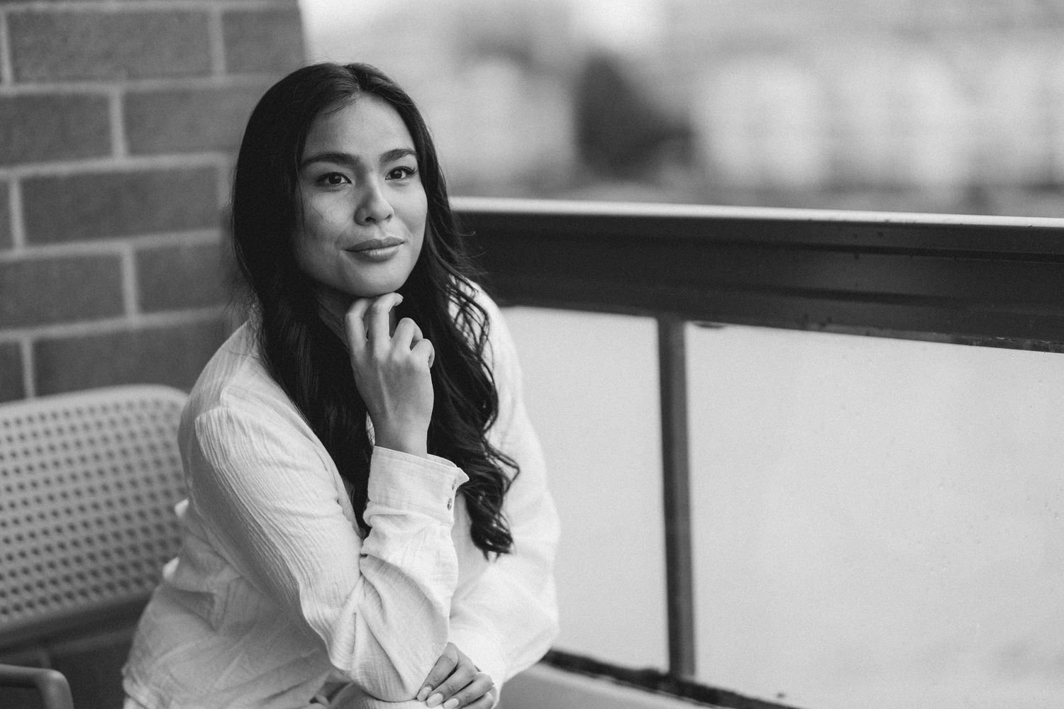 A portrait in black and white of someone in a white shirt sitting by a window with thoughtful expression.