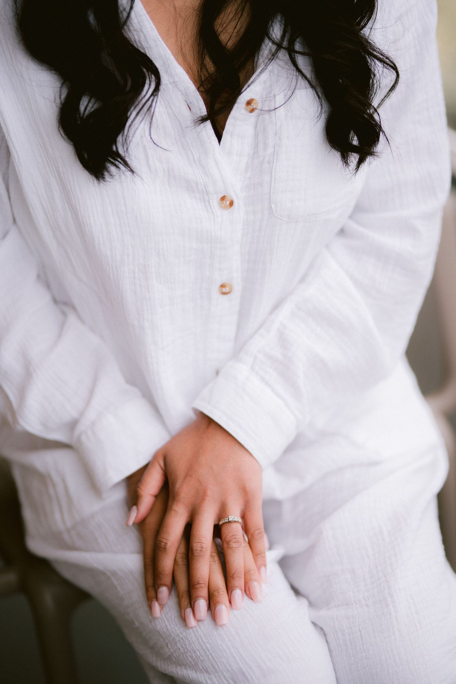 Close-up of hands wearing an engagement ring with a white linen button-down shirt.