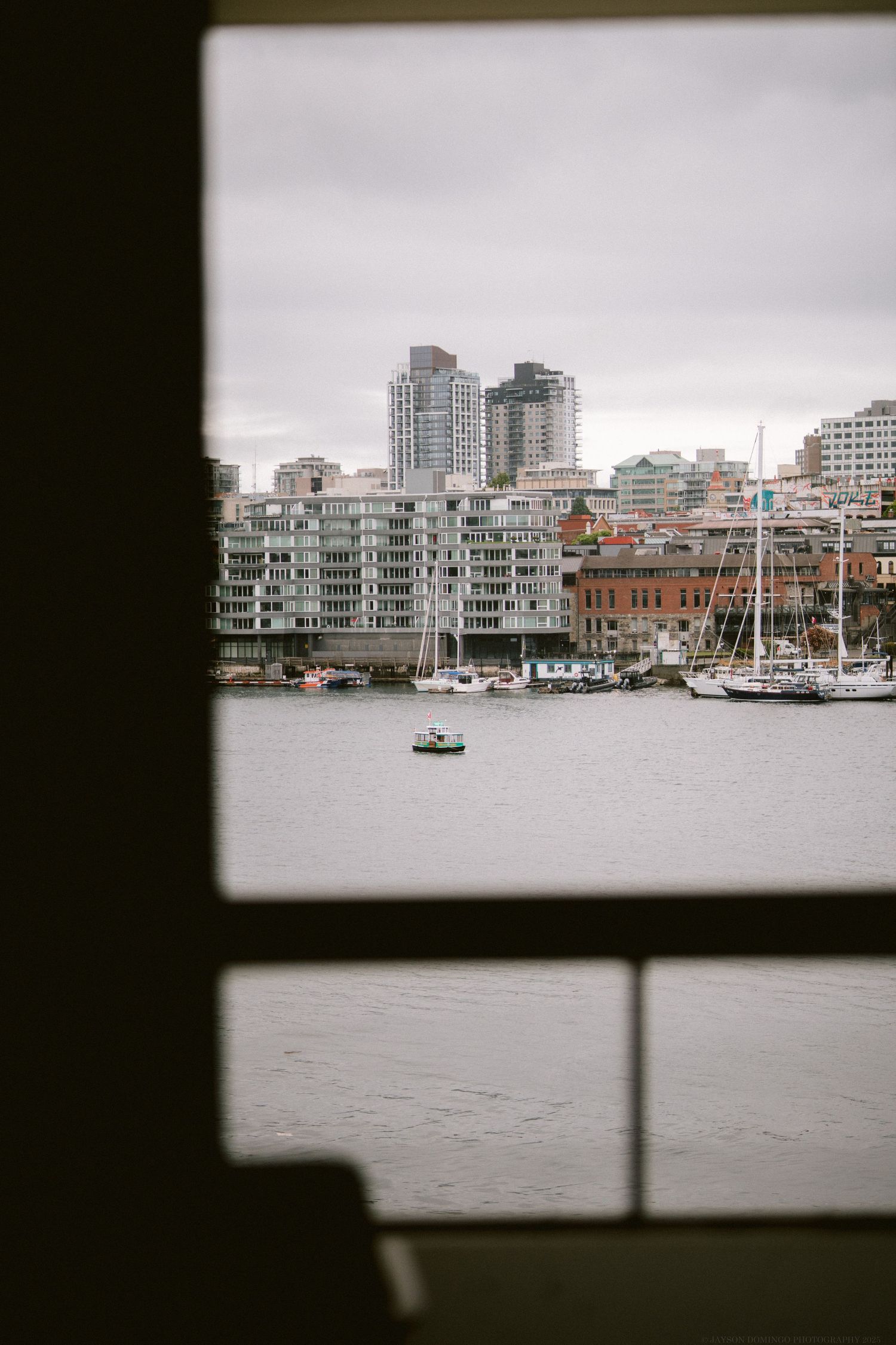 View of waterfront buildings and boats through a window frame in an urban harbor setting.