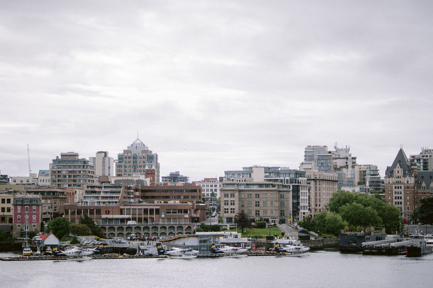 Victoria harbor skyline with boats and historic buildings under cloudy skies.