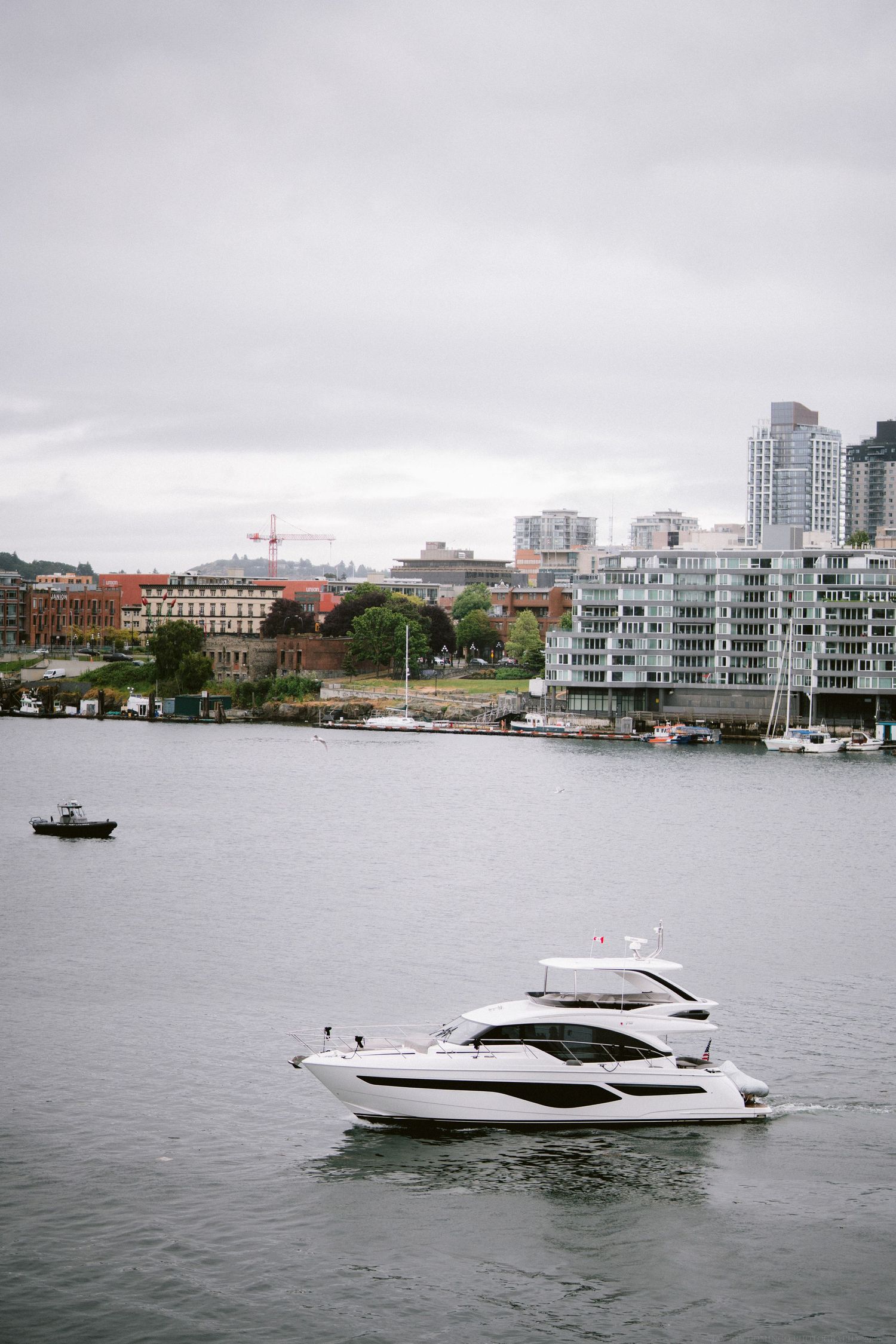 Luxury yacht cruises past waterfront condominiums and marina on an overcast day.
