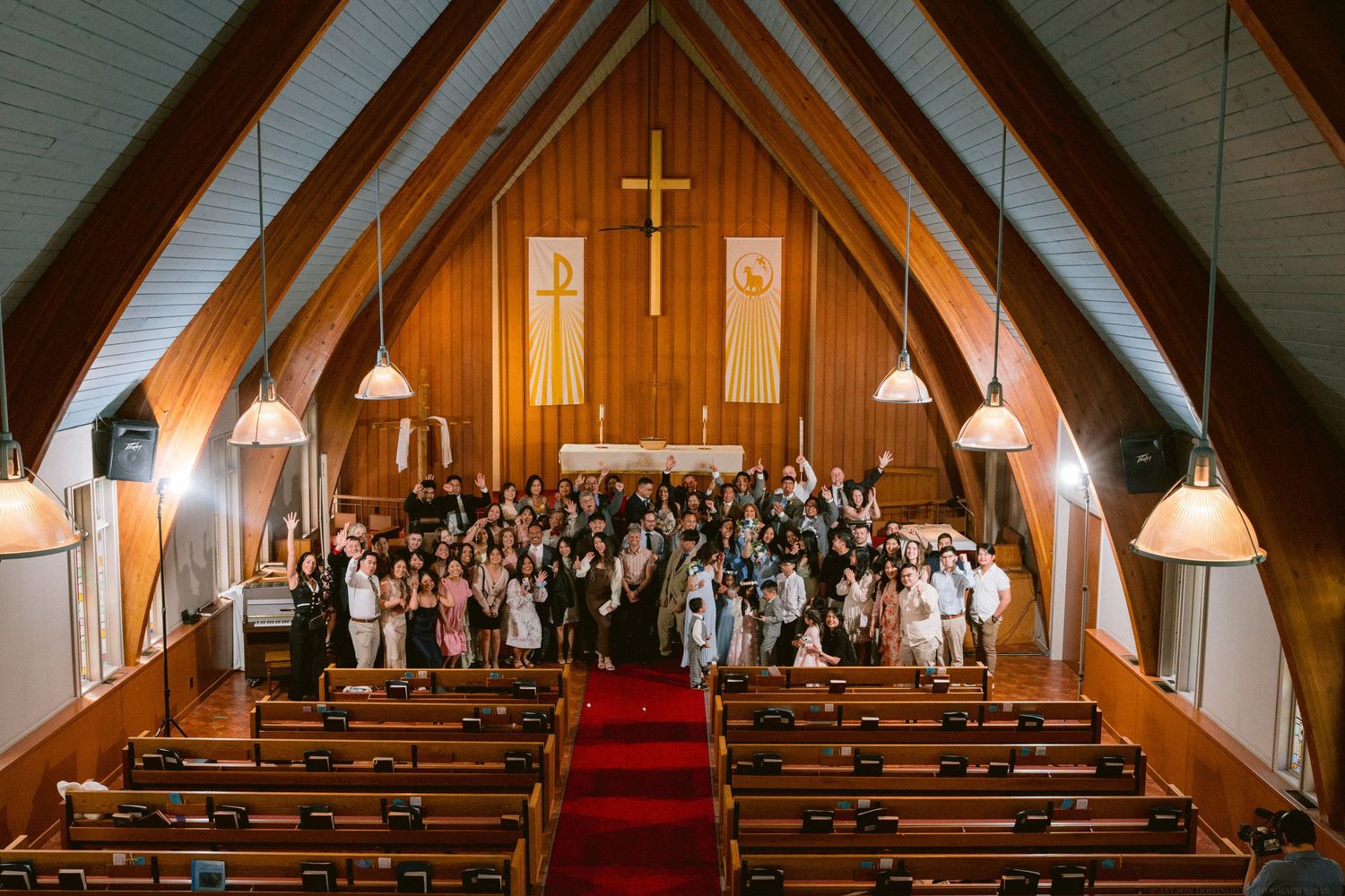 Wedding guests fill the pews of a traditional church with vaulted wooden ceilings and warm lighting.