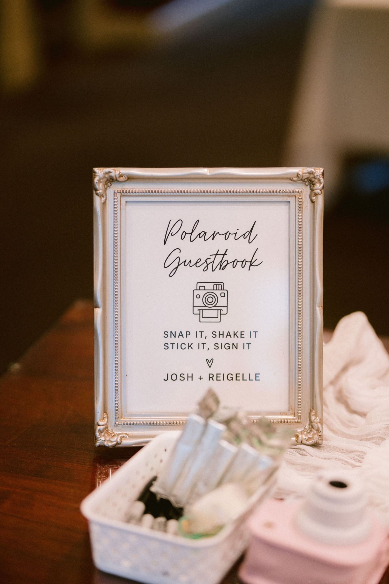 Vintage-styled polaroid guestbook sign in an ornate frame at a wedding reception.