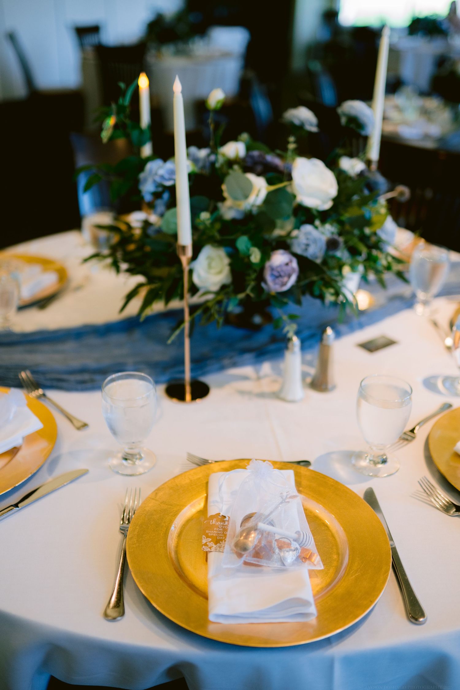 Elegant wedding reception table setting with gold chargers and floral centerpiece.