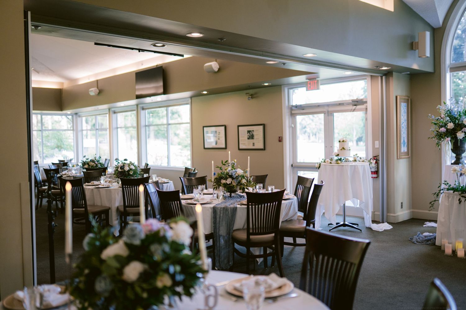 An elegant wedding reception venue with round tables, white linens and natural lighting from large windows.