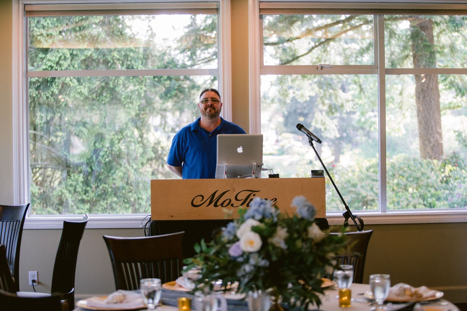 DJ setup at wedding reception with laptop and equipment near bright windows.
