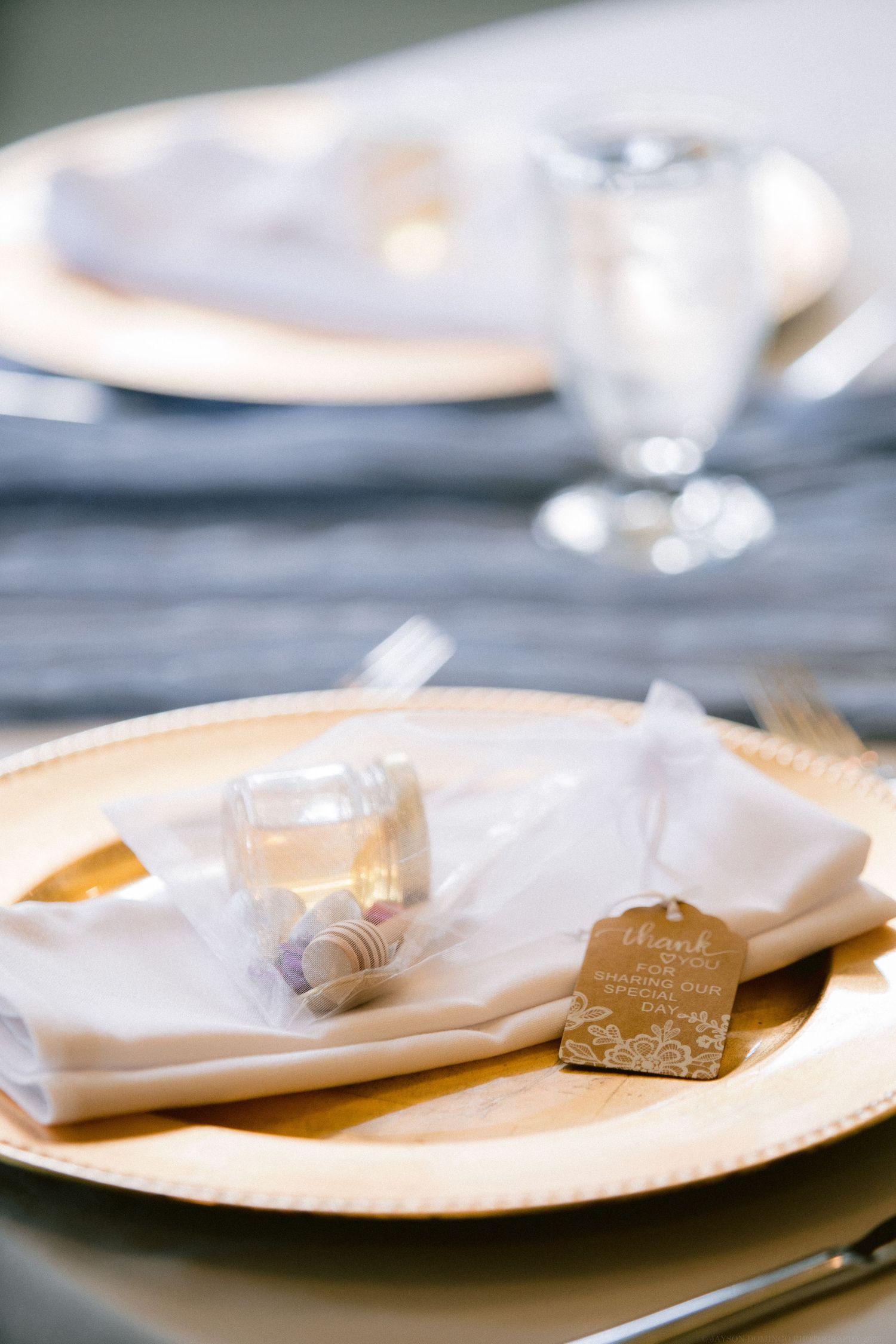 Elegant place setting with gold charger plate, white napkin and wedding favor.