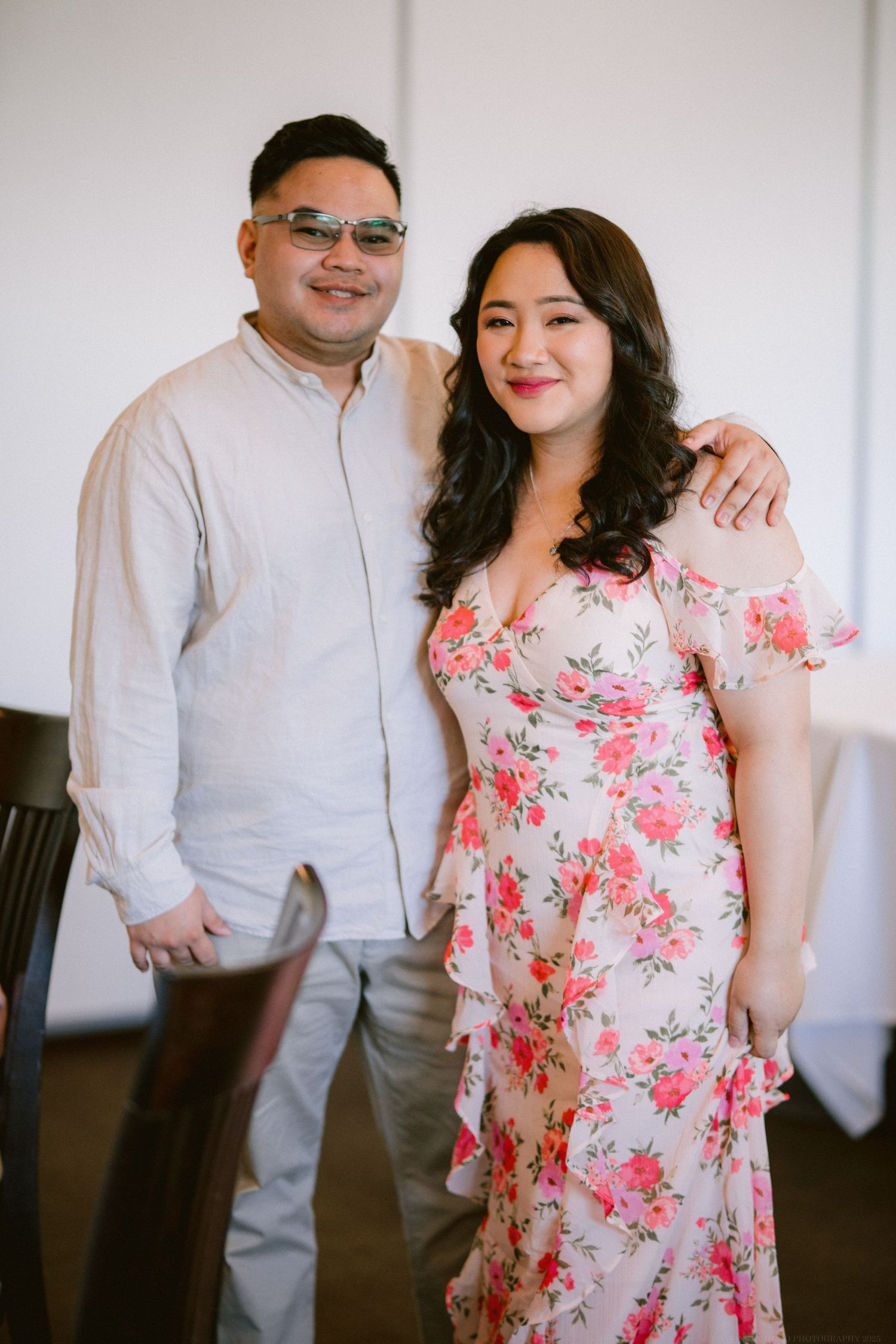 Couple poses together in formal wear with floral dress and light colored outfit.
