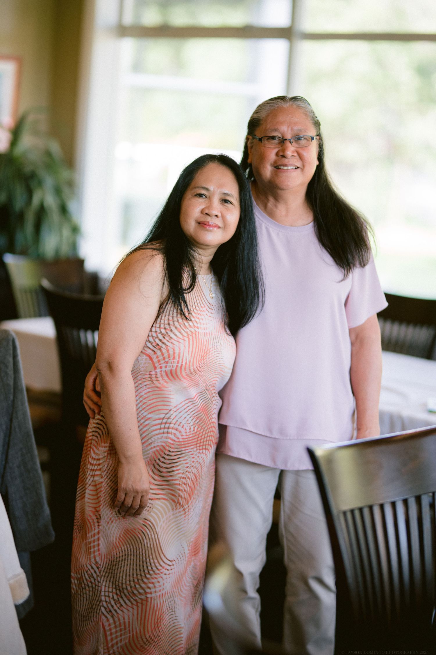 Two people in coordinating pink and white outfits pose together in a sunlit room.