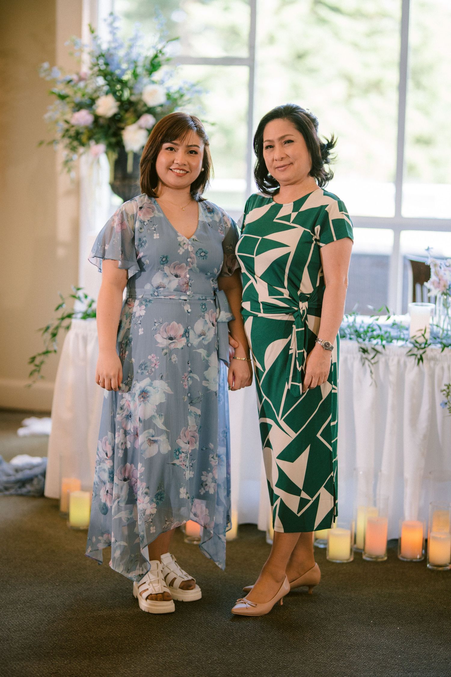 Two women in floral and geometric print dresses pose together at an elegant wedding reception.