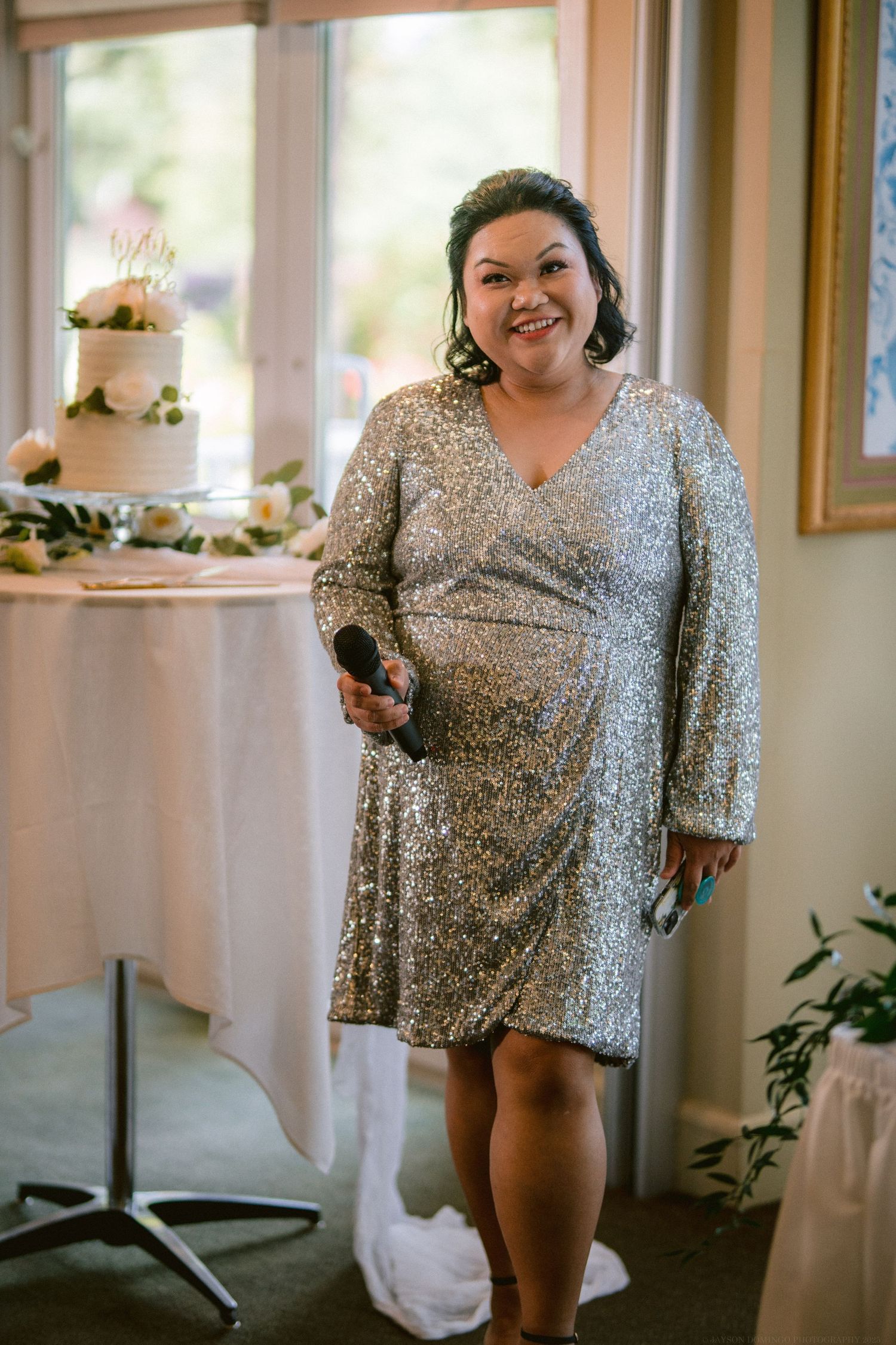 Person in sparkly silver dress stands next to wedding cake at reception.