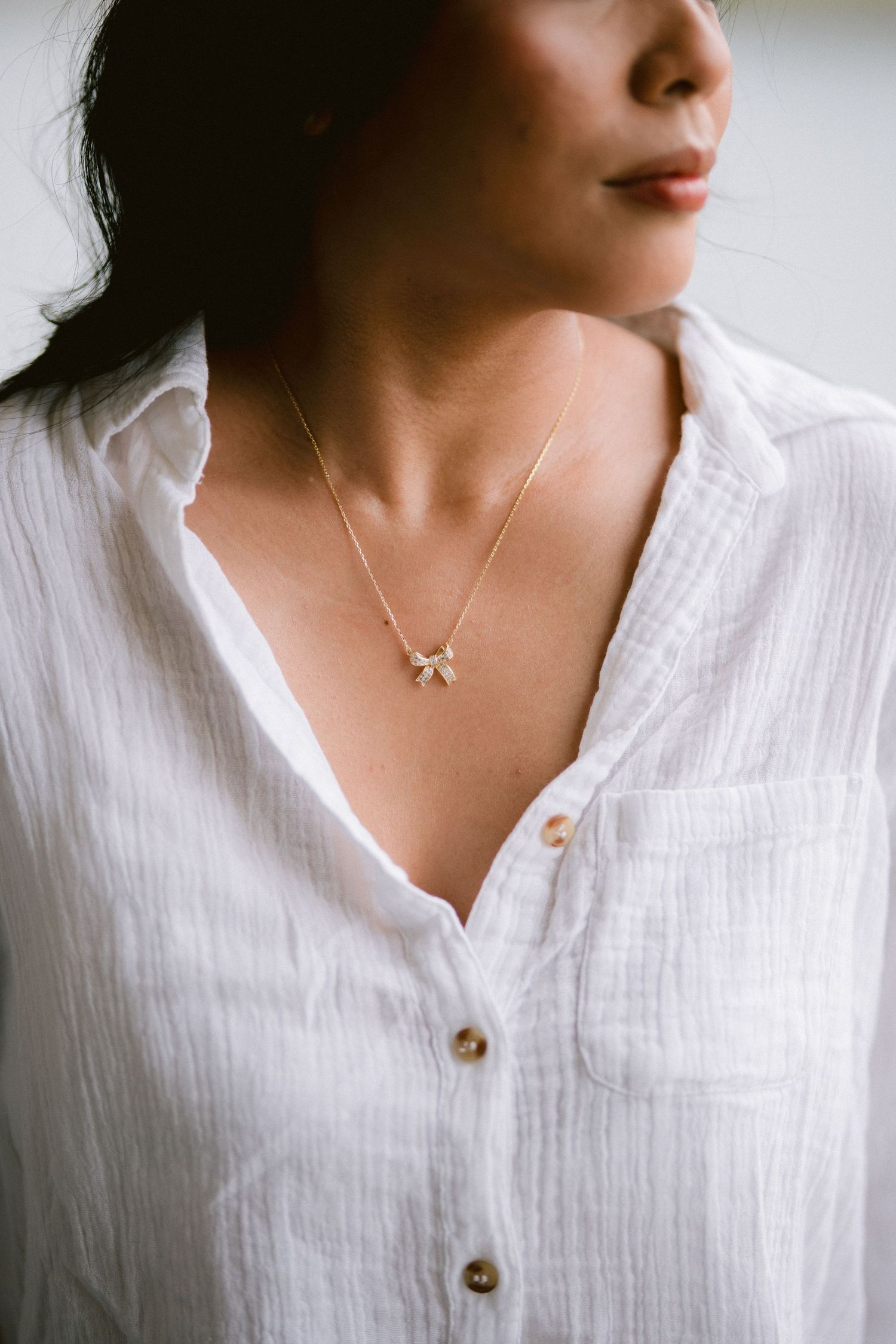 Close-up views of a delicate white necklace worn with a crisp white button-up linen shirt.