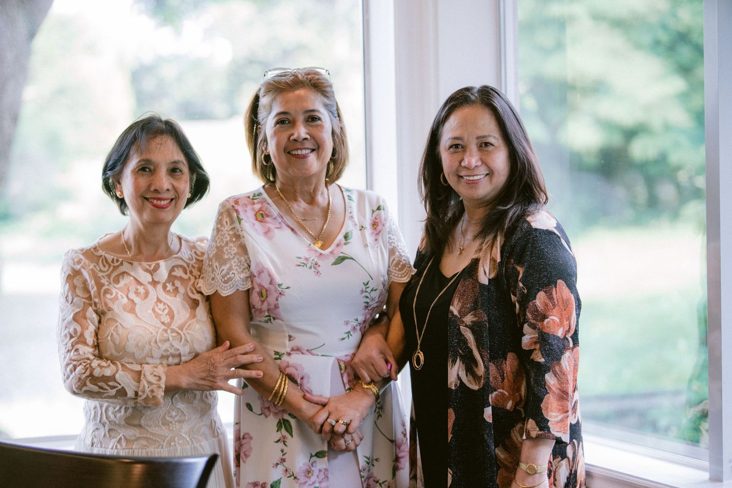 Three elegantly dressed women in floral dresses pose together at a formal event.