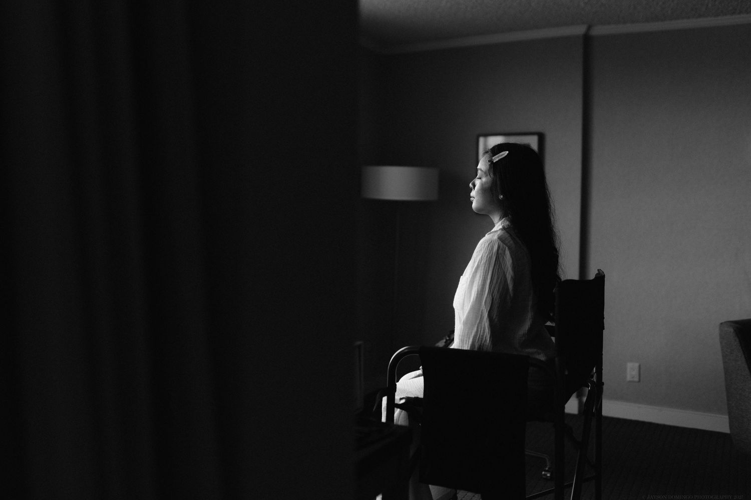 A dramatic black and white silhouette of someone sitting in a chair during wedding preparations.