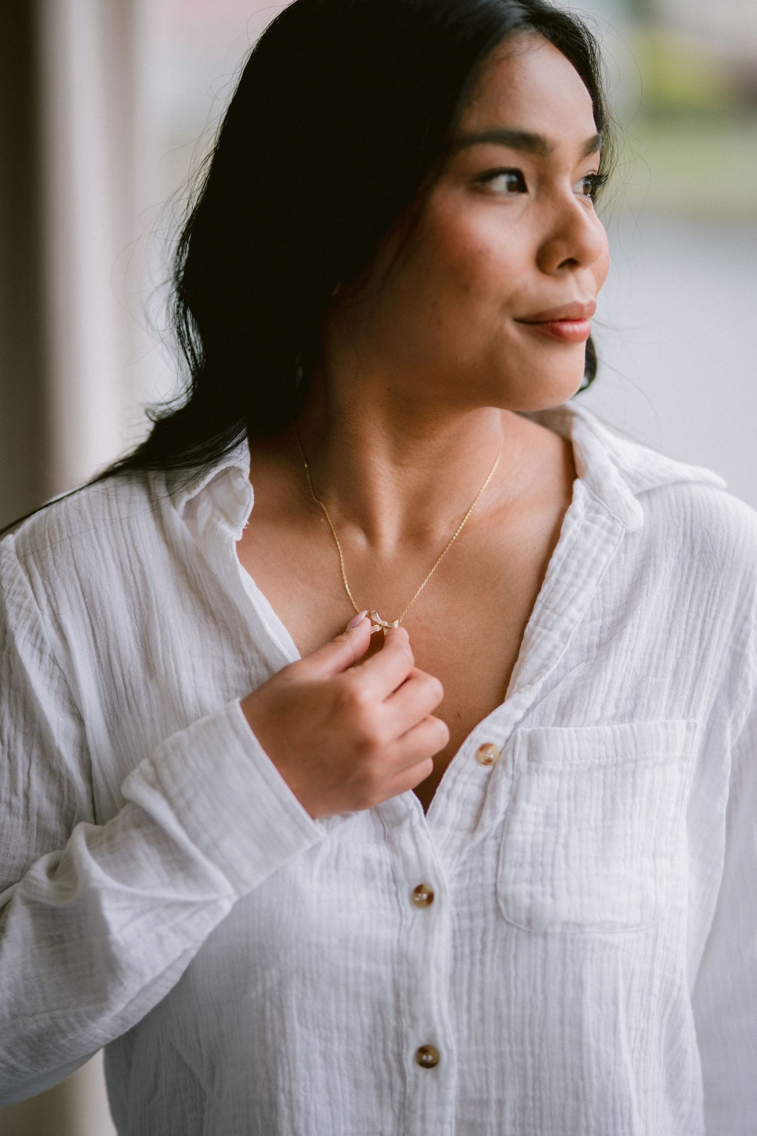 Side profile portrait showing delicate necklace against a white button-down shirt.
