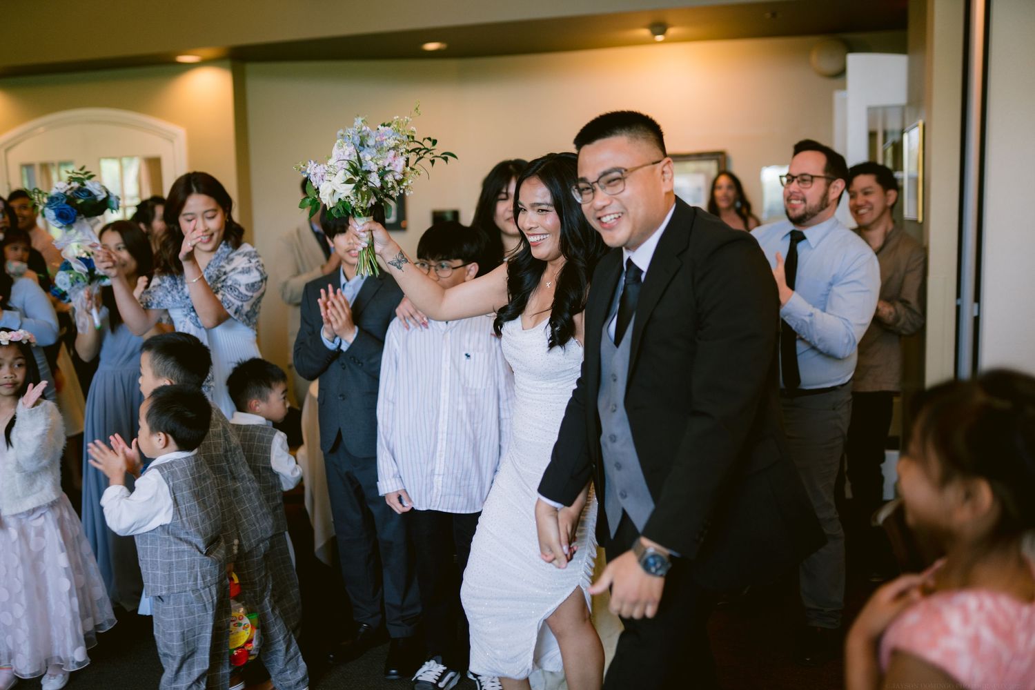 Guests celebrate and take photos during a wedding reception in an indoor venue.