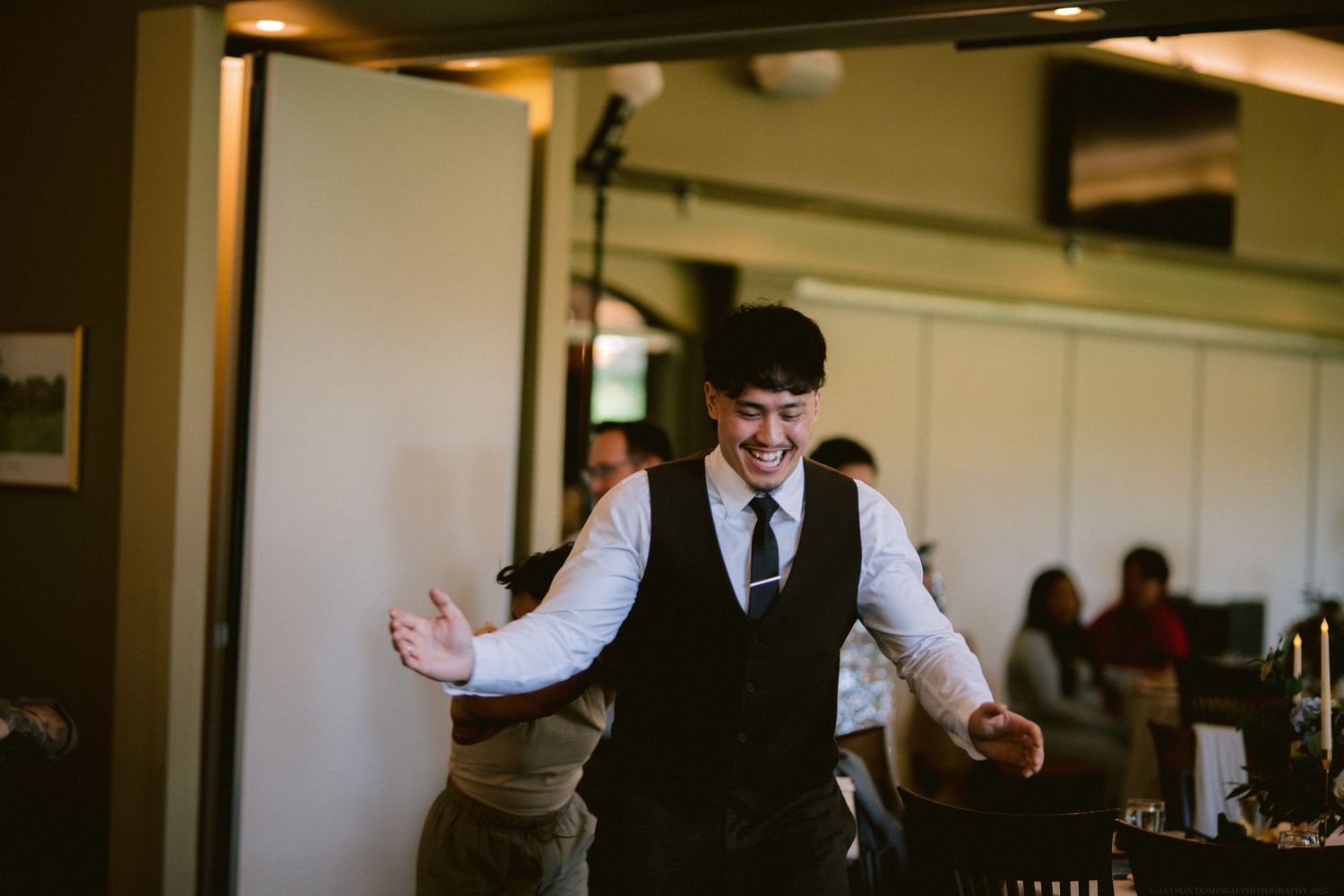 A bartender in formal attire gestures expressively while working at an indoor venue during an event.
