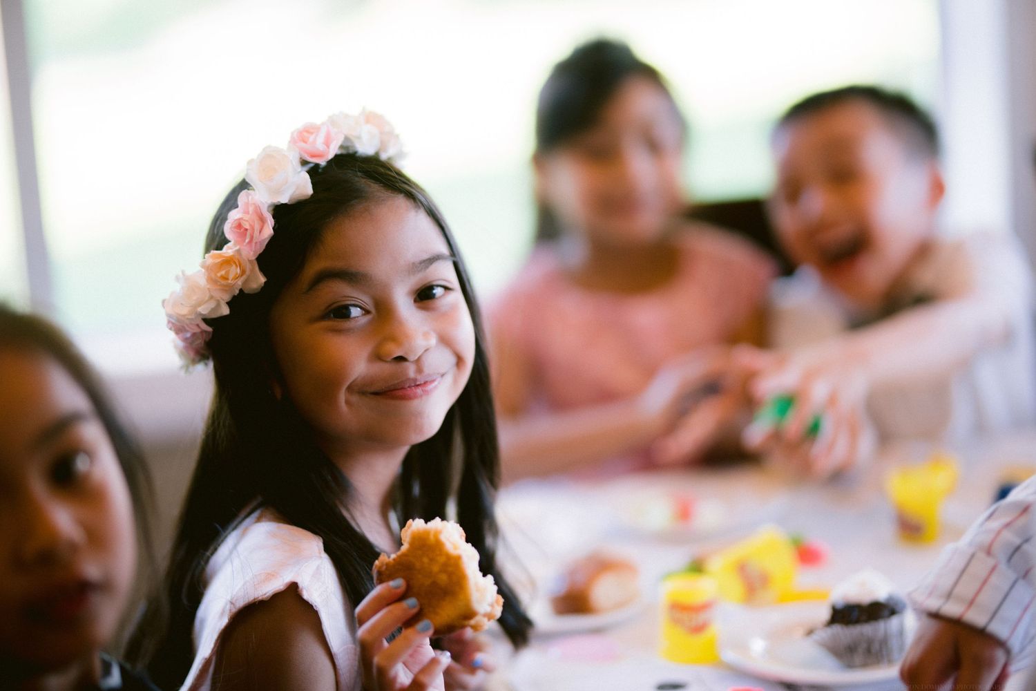 Young guest wearing a floral crown enjoys food at a celebratory gathering.