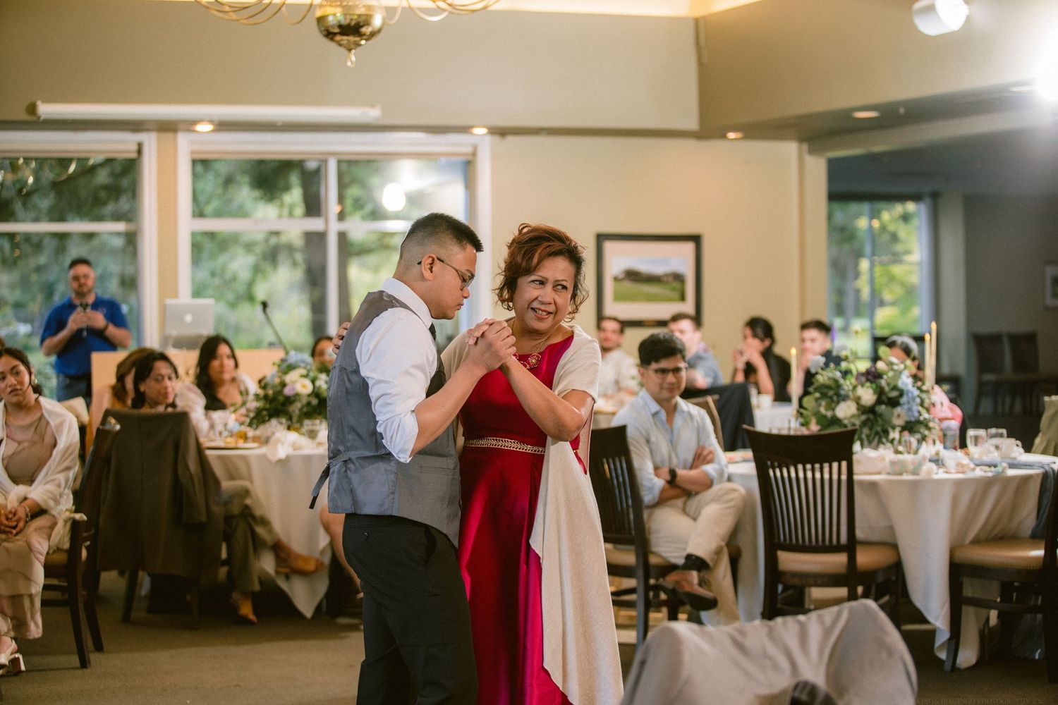 Wedding guests share a dance on the reception floor as others watch from tables.