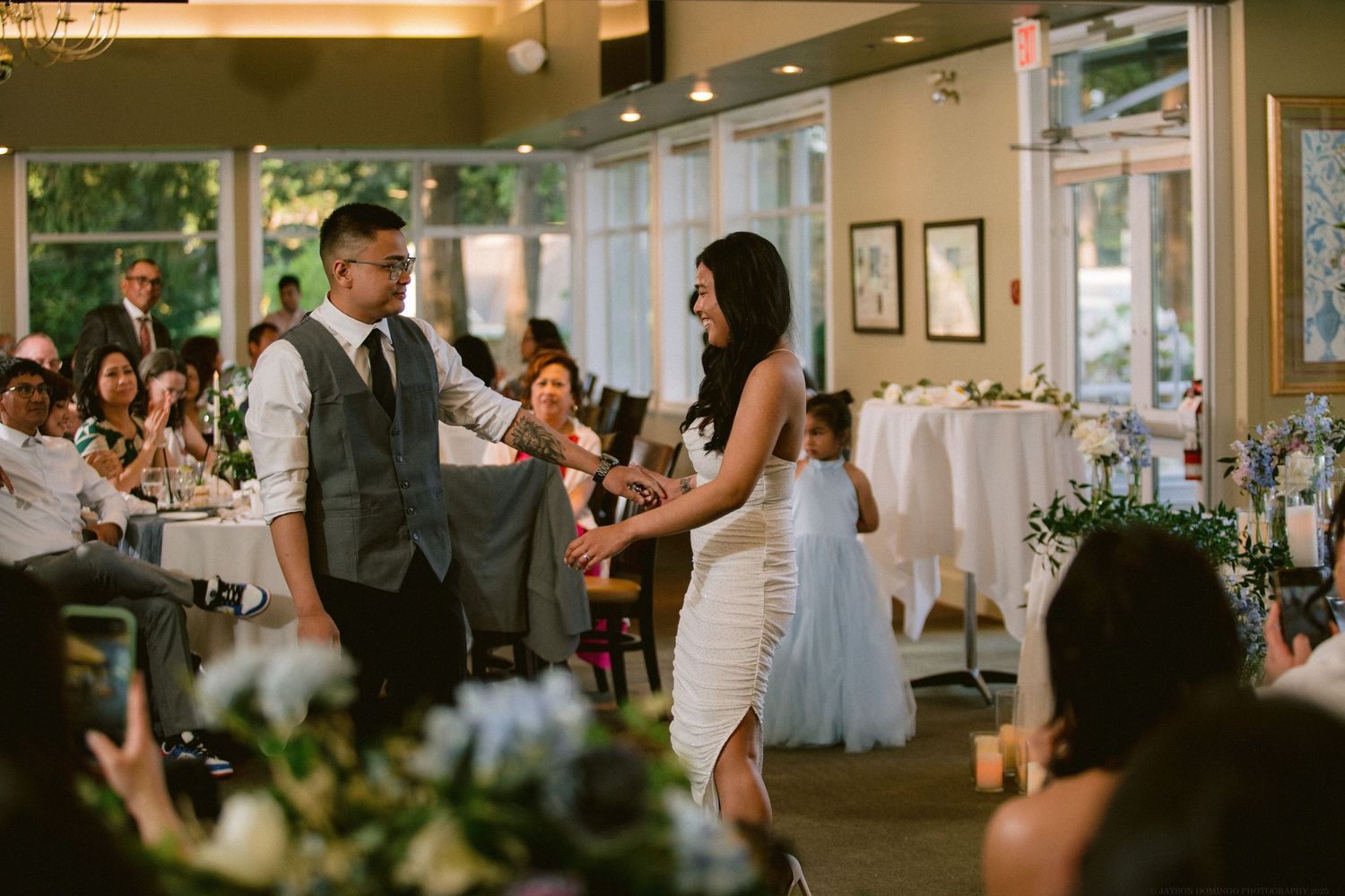 Guests dance at a wedding reception venue decorated with floral arrangements and elegant table settings.