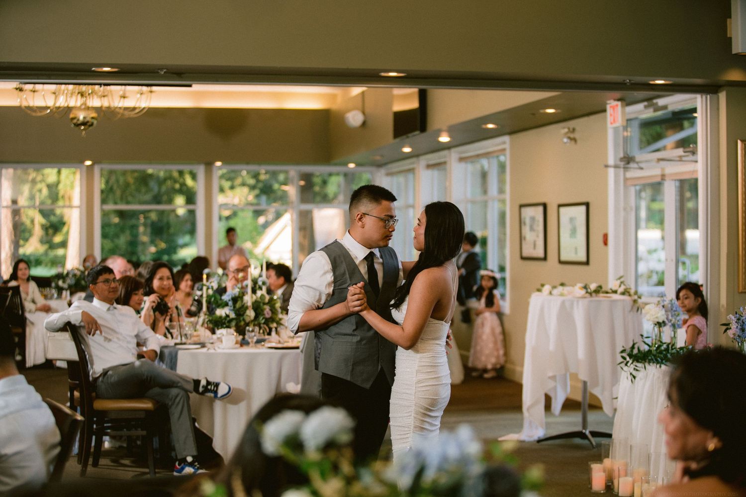 Couple shares first dance at wedding reception surrounded by decorated tables and guests.