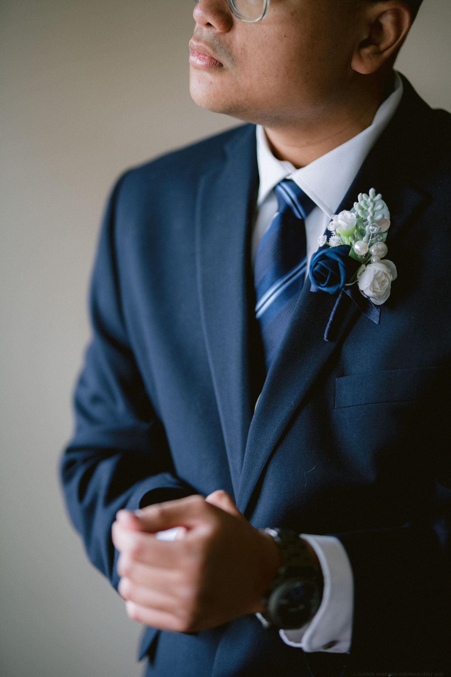 A close-up detail of a navy blue suit with a blue striped tie and white floral boutonniere.